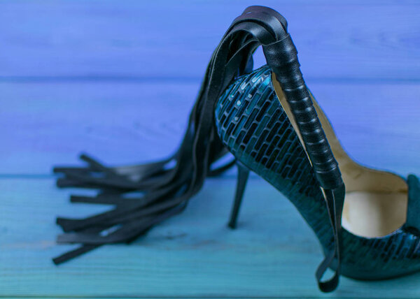 A whip and a heel on a wooden background. BDSM concept.