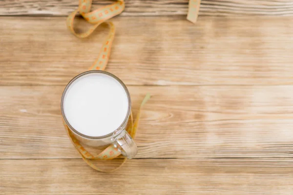 Een glas melk (kefir) en een meetband op een houten achtergrond. Het concept van dieet, verlies van het gewicht. — Stockfoto