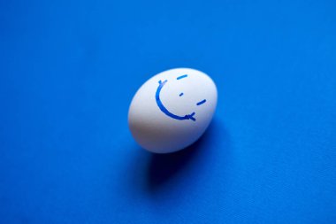 Mavi arka planda komik bir gülücük olan beyaz bir yumurta..