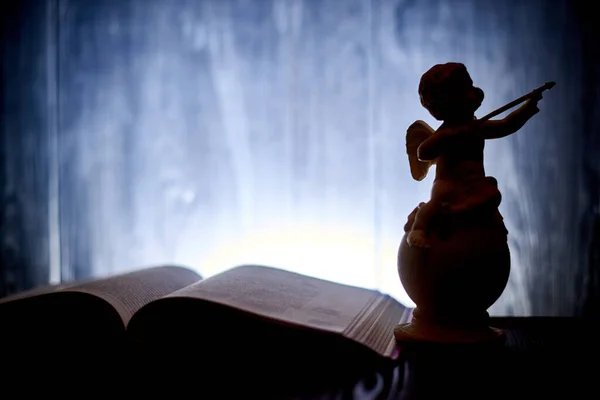 丘比特的形象 一个天使 在黑暗闪耀的背景下 在一本打开的书旁边 带着弓 案文的位置 — 图库照片
