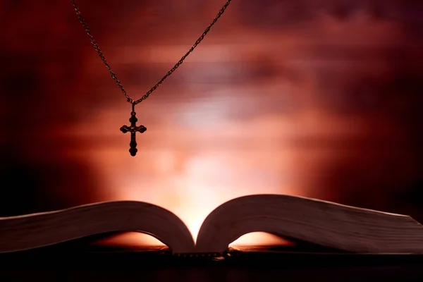 An open bible and a church cross in dark colors and a shining background.