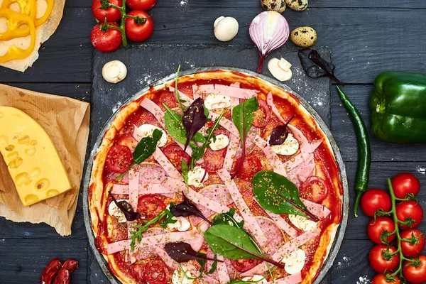 Raw pizza with mozzarella cheese, meat, tomatoes, mushrooms, peppers, herbs on a dark wooden background. Cooking delicious italian pizza.