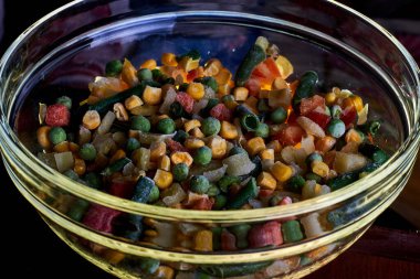 Donmuş farklı sebzeler, ahşap bir zeminde cam bir tabakta..