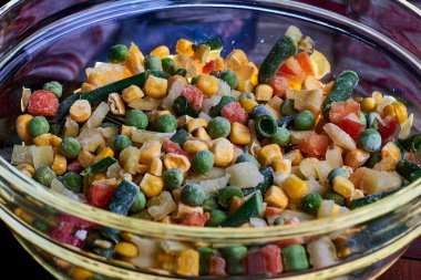 Donmuş farklı sebzeler, ahşap bir zeminde cam bir tabakta..