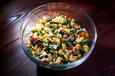 Donmuş farklı sebzeler, ahşap bir zeminde cam bir tabakta..