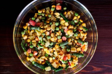 Donmuş farklı sebzeler, ahşap bir zeminde cam bir tabakta..