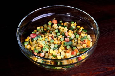 Donmuş farklı sebzeler, ahşap bir zeminde cam bir tabakta..