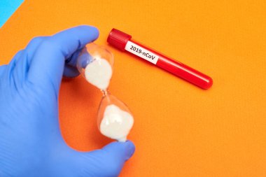 Coronavirus, üzerinde kan ve turuncu bir arka planda lastik eldiven bulunan bir test tüpündeki yazıt..