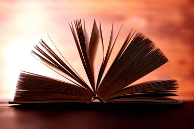 Kahverengi arka planda ışıkla aydınlatılmış, kalın bir kitap..