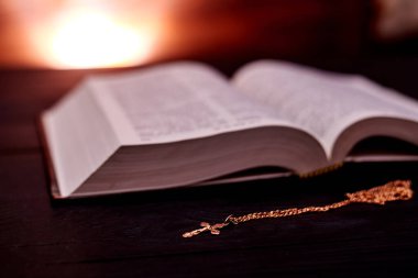 Açık bir İncil ve koyu renklerde bir kilise haçı ve parlak bir arka plan..