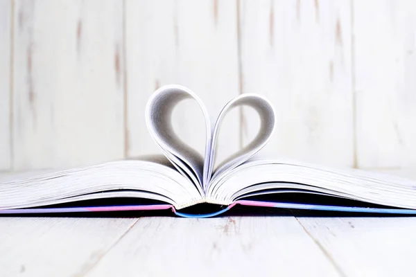 An open book with a folded heart from the old ladies on a light wooden background.