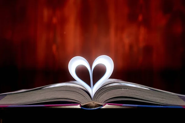 A heart from book pages shines in on a brown background.