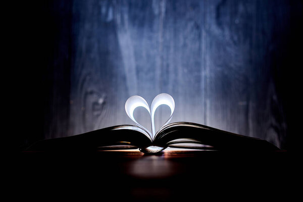 A heart from book pages shines in the dark.