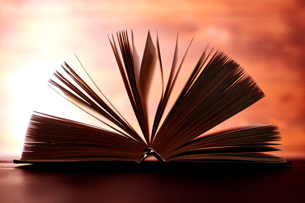 An opened thick book backlit by light on a brown background.