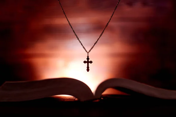 暗い色と輝く背景で開かれた聖書と教会のクロス — ストック写真