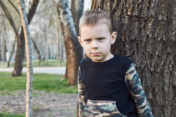 O menino está severamente perto da árvore. . — Fotografia de Stock