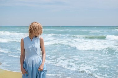 Okyanus kıyısında mavi elbiseli sarışın bir kadın. Yaz tatili, seyahat, tatil kavramı..