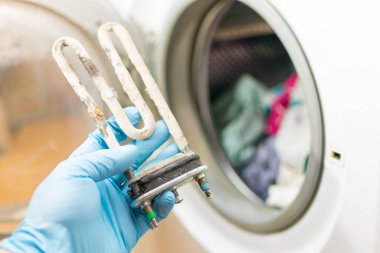 Çamaşır makinesi tamiri. Türbüler elektrikli ısıtma elementi ile tamircinin eli