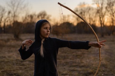 Doğada gün batımının ışınlarında elinde ev yapımı yay olan bir kız..