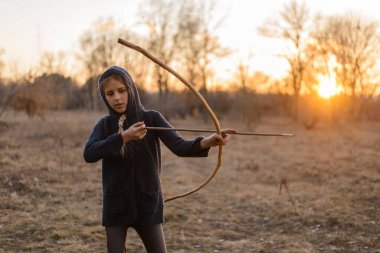 Doğada gün batımının ışınlarında elinde ev yapımı yay olan bir kız..