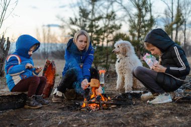 Anne, kız ve oğul piknikte kamp ateşinin etrafında oturuyorlar. Aile açık hava eğlencesi. Seyahat, yürüyüş, konsepti durdurmak.