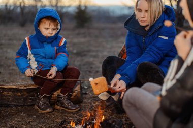 Anne, kız ve oğul piknikte kamp ateşinin etrafında oturuyorlar. Aile açık hava eğlencesi. Seyahat, yürüyüş, konsepti durdurmak.
