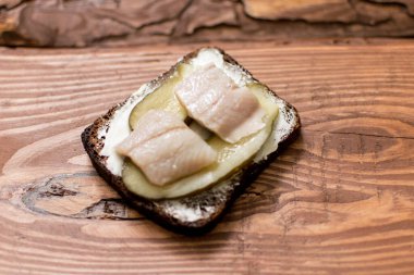 Tahta arka planda tereyağlı ve ringa balıklı siyah ekmekten yapılmış sandviç..