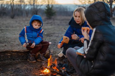 Anne, kız ve oğul piknikte kamp ateşinin etrafında oturuyorlar. Aile açık hava eğlencesi. Seyahat, yürüyüş, konsepti durdurmak.