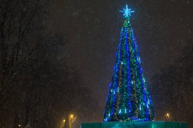 Noel ağacı süslenmiş sokak çelenkleri, gece parkta kar yağarken parlıyor..