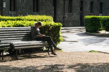 Telefonu olan genç kız bankta oturuyor..