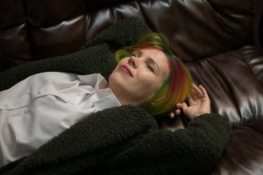 Çok renkli saçlı bir kadın deri bir kanepede yatıyor..