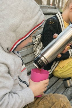 Küçük bir çocuk bankta çay içiyor..