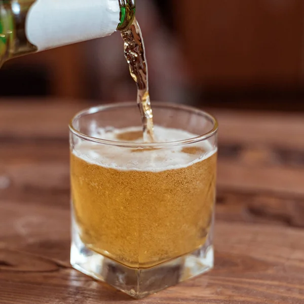 Beer is poured into a glass from a bottle on a wooden background.