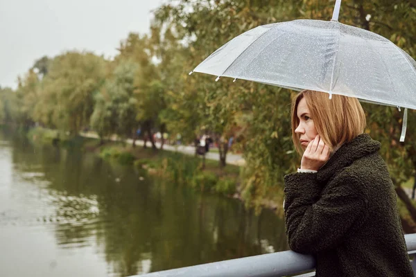 Woman under an umbrella in the fall in a park near a pond. Autumn landscape, rain, bad weather.