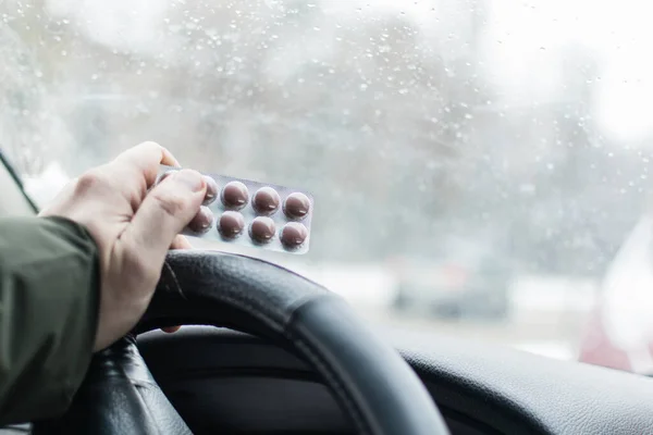İlaç ve araba kullanma. Erkek el, direksiyonda haplarla su toplamış..