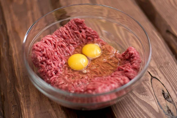 Fresh minced meat with chicken eggs on a plate on a wooden background for cooking.
