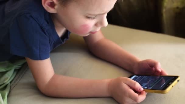 Ένα Μικρό Αγόρι Κοιτάζει Τηλέφωνο Ενώ Βρίσκεται Έναν Καναπέ — Αρχείο Βίντεο
