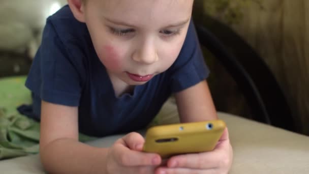 Niño Pequeño Mira Teléfono Mientras Está Acostado Sofá — Vídeos de Stock