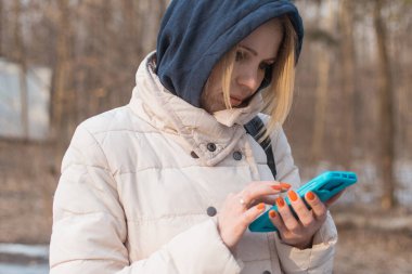 Elinde cep telefonu olan, sokakta ceketi olan bir kadın..