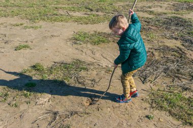 Küçük bir çocuk bir sopayla toprağı kazıyor..