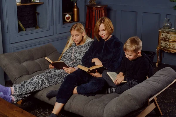 Mom with two children read books while sitting on the couch. Family reading paper books.