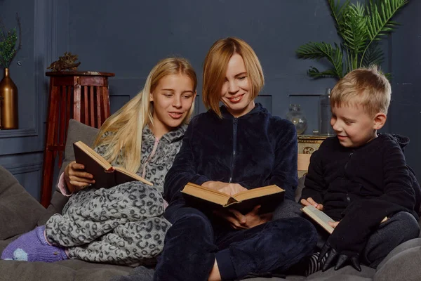 Mom with two children read books while sitting on the couch. Family reading paper books.