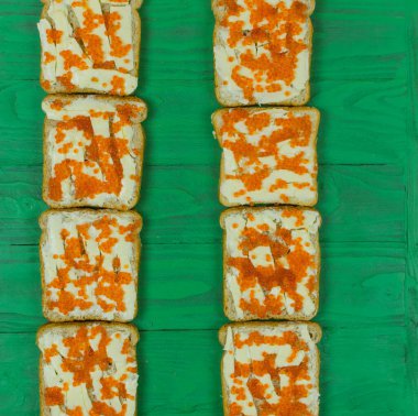 Açık yeşil ahşap arka planda kırmızı havyarlı sıra sıra sandviç..