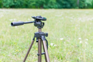 Yeşil bir açıklıkta duran kamera için bir tripod..