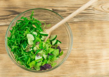 Taze marul yaprakları, fesleğen, ahşap arka planda cam bir kasede roka. Vejetaryen sebze salatası hazırlığı.