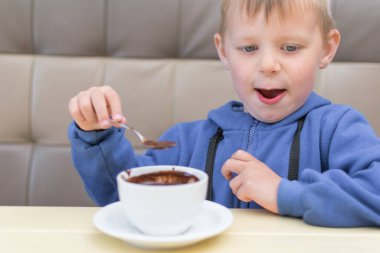 3-5 yaşlarında küçük bir çocuk bir kafede sıcak çikolata yiyor..