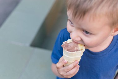 Küçük bir çocuk dondurma yiyor. Çocuk waffle bardağında limonlu çikolatalı dondurma yiyerek uzaklaşıyor. Bebek lezzeti..