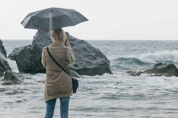 Kadın depresyonu, yalnızlık konsepti. Kadın yağmurda şemsiyenin altında taşların ve heyecan verici denizin altında..