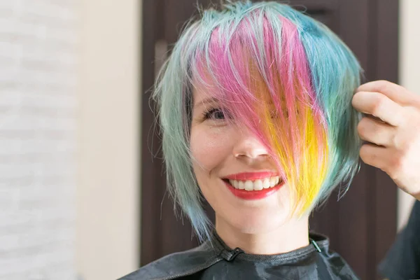 Woman 30-40 smiles and made coloring of hair in different colors in a hairdressing salon. Change the image of a woman.