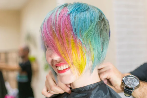 Woman 30-40 smiles and made coloring of hair in different colors in a hairdressing salon. Change the image of a woman.